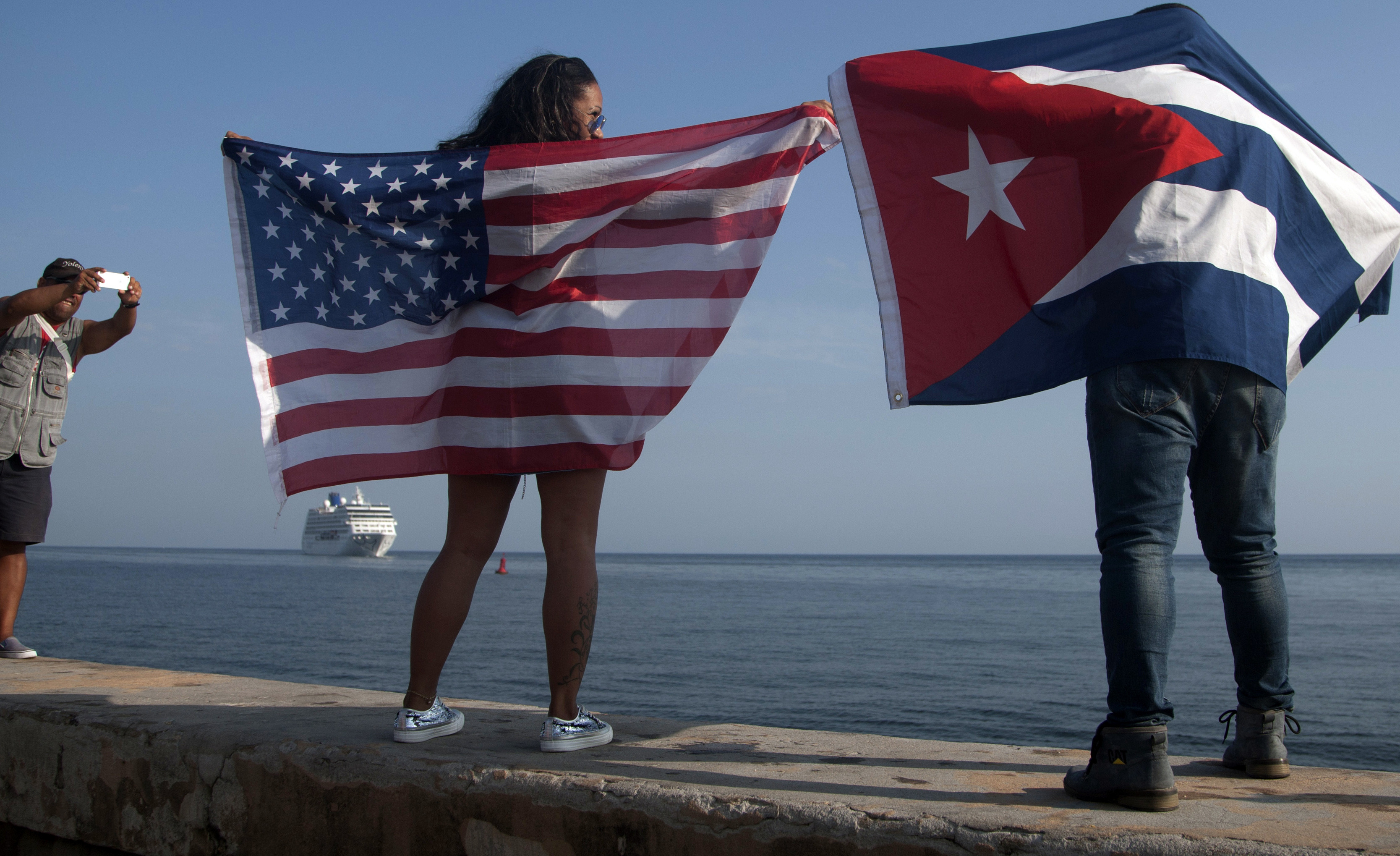In this May 2, 2016 file photo, Yaney Cajigal, left, holds out a Stars and Stripes, and Dalwin Valdes holds a Cuban national flag, as they watch the arrival of Carnival's Adonia cruise ship from Miami, in Havana, Cuba, the first step toward a future in which thousands of ships a year could cross the Florida Straits, long closed to most U.S.-Cuba traffic. A rare 2016 poll of Cuban public opinion has found that most Cubans approve of normal relations with the United States and large majorities want more tourism and private business ownership. (AP Photo/Fernando Medina, File) (AP)