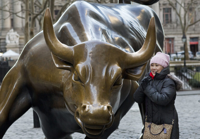 In this March 23, 2017 photo, a woman poses for photos with the Charging Bull statue in New York. Since 1989 the massive, bronze bull has stood in New York City's financial district as an image of the might and hard-charging spirit of Wall Street. (AP Photo/Mark Lennihan) (AP)