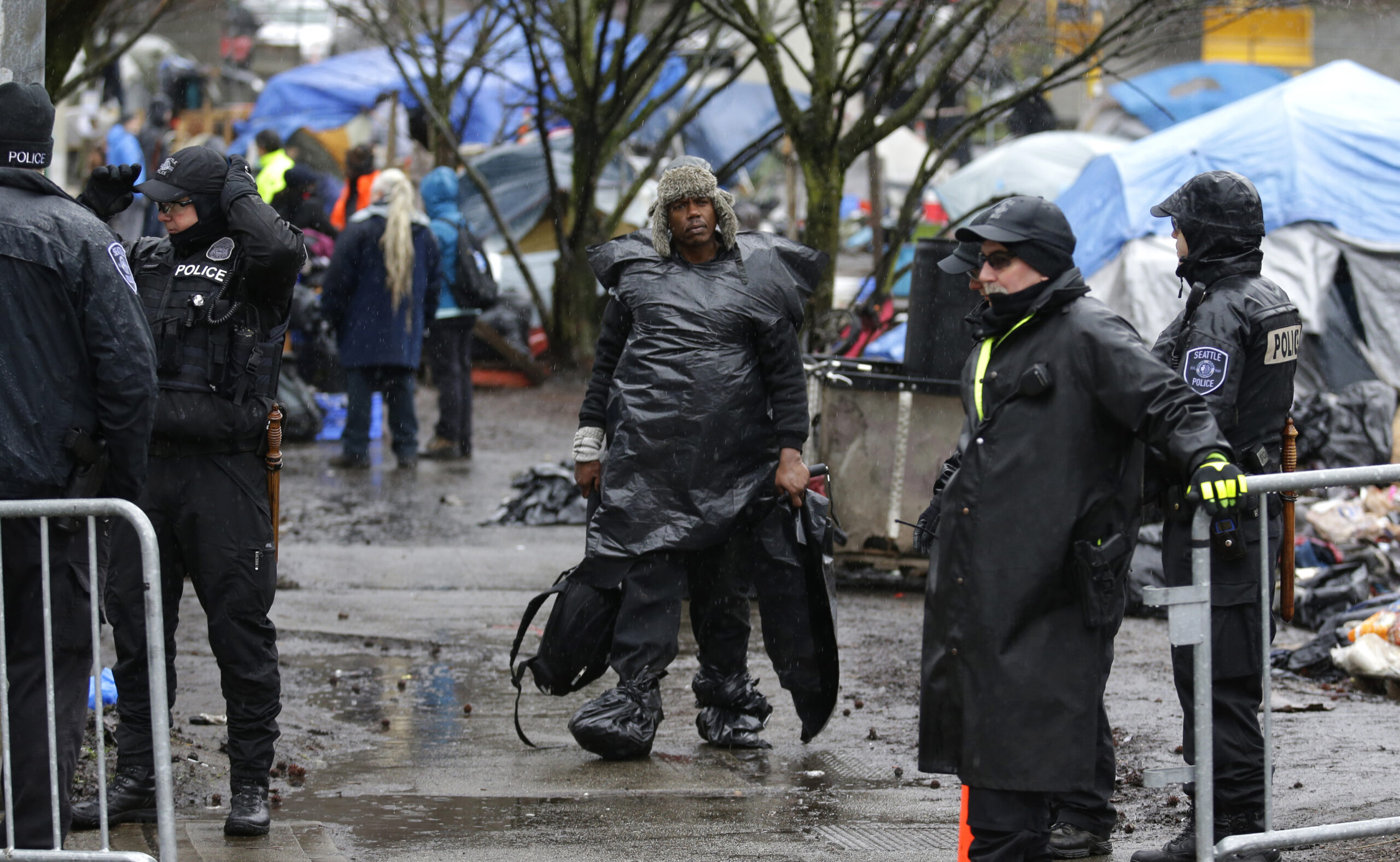 In this March 7, 2017 photo, a man wearing plastic bags in the rain carries belongings as he walks during a sweep to clear out people living at a homeless encampment known as "The Field," in Seattle's Stadium district south of downtown. Sixteen months after he declared a state of emergency on homelessness, Seattle’s mayor is asking voters in this liberal, affluent city for $55 million a year in new taxes to fight the problem. (AP Photo/Ted S. Warren) (AP)