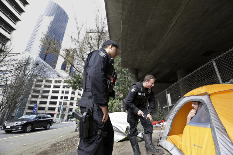 In this photo taken Thursday, March 23, 2017, Seattle police officers Wes Phillips, left, and Tori Newborn talk with Corvin Dobschutz as part of a new team of outreach workers and officers that go out and connect homeless people to services, as the homeless man sits in his tent below a freeway and next to downtown Seattle. (AP Photo/Elaine Thompson) (AP)