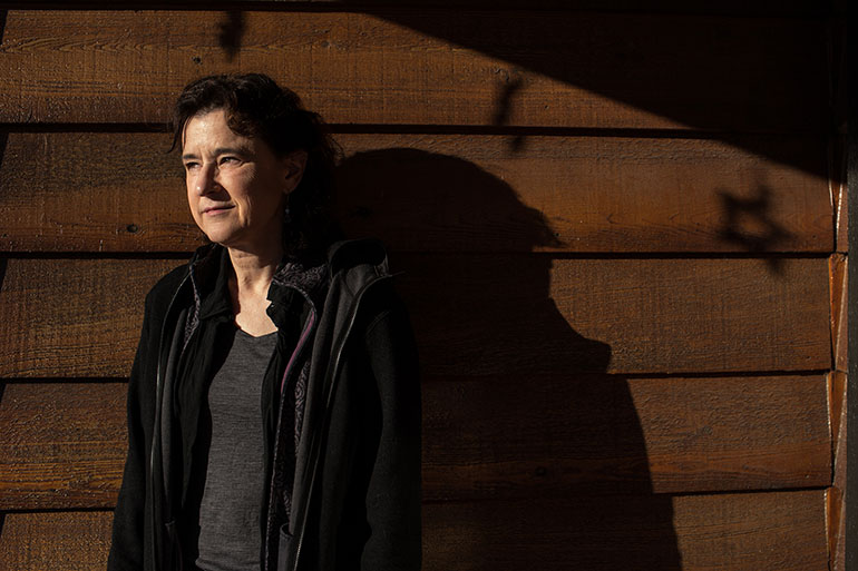 Jen Jolliffe, 55, poses outside her home in Anchorage, Alaska. Jolliffe, an acupuncturist, works from home with her boyfriend, Andrew Hawk, 52, a gunsmith.  Both receive health care coverage through the ACA and are concerned about what a GOP plan for health coverage would mean for them. (Ash Adams/Kaiser Health News)