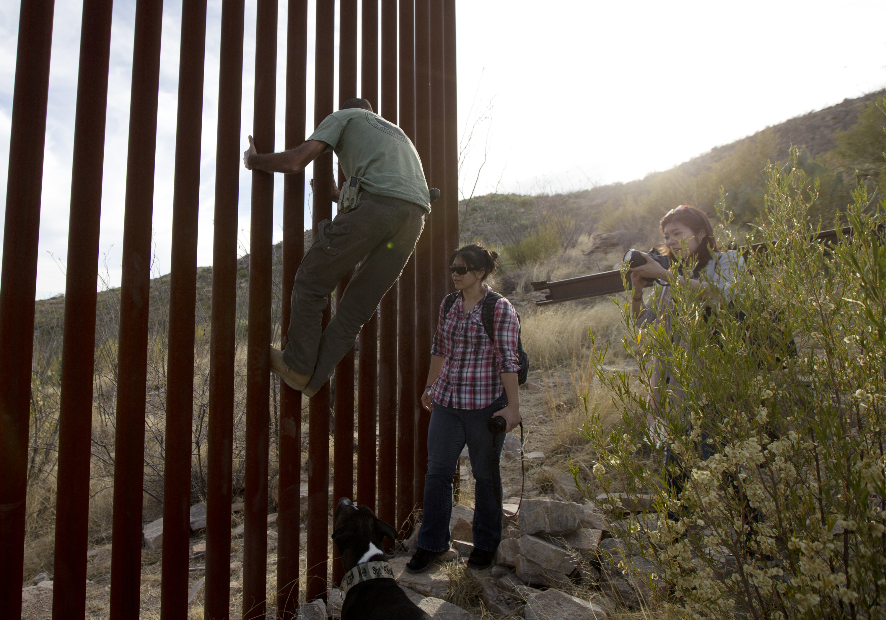 FILE - In this May 11, 2016, file photo, Tim Foley shows how to climb a section of the border wall separating Mexico and the United States near where it ends as journalists Chitose Nakagawa, right, and Marcie Mieko Kagawa look on in Sasabe, Ariz. Foley, a former construction foreman, founded Arizona Border Recon, a group of armed volunteers who dedicate themselves to border surveillance. With bids due Tuesday, April 4, 2017, on the first border wall design contracts, companies are preparing for the worst if they get the potentially lucrative but controversial job. (AP Photo/Gregory Bull, File) (AP)