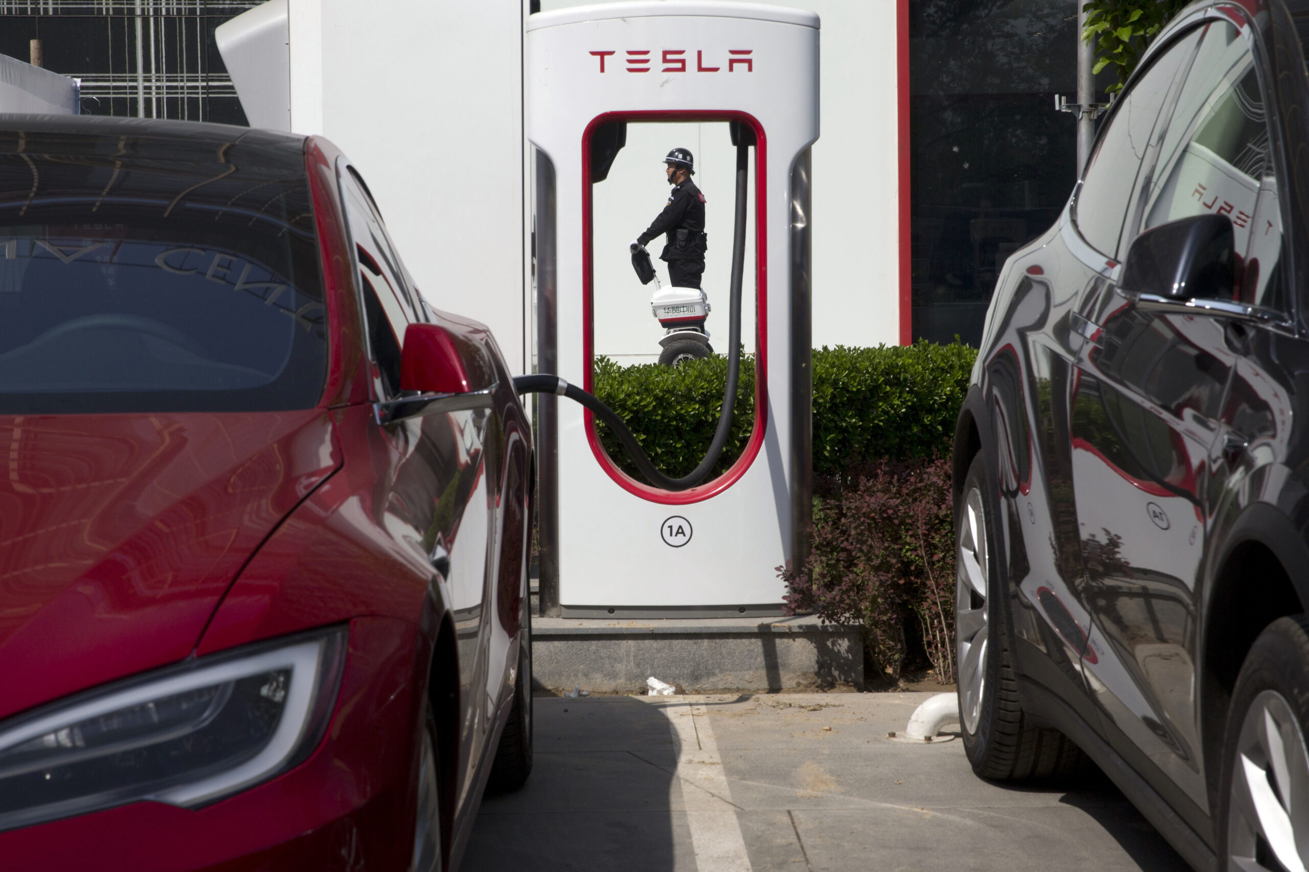 In this Friday, April 14, 2017 photo, a security personnel riding a motorized platform moves past an electric vehicle charging station in Beijing, China. Automakers face a conflict in China's huge but crowded market: Regulators are pushing them to sell electric cars, but buyers want gasoline-hungry SUVs. (AP Photo/Ng Han Guan)