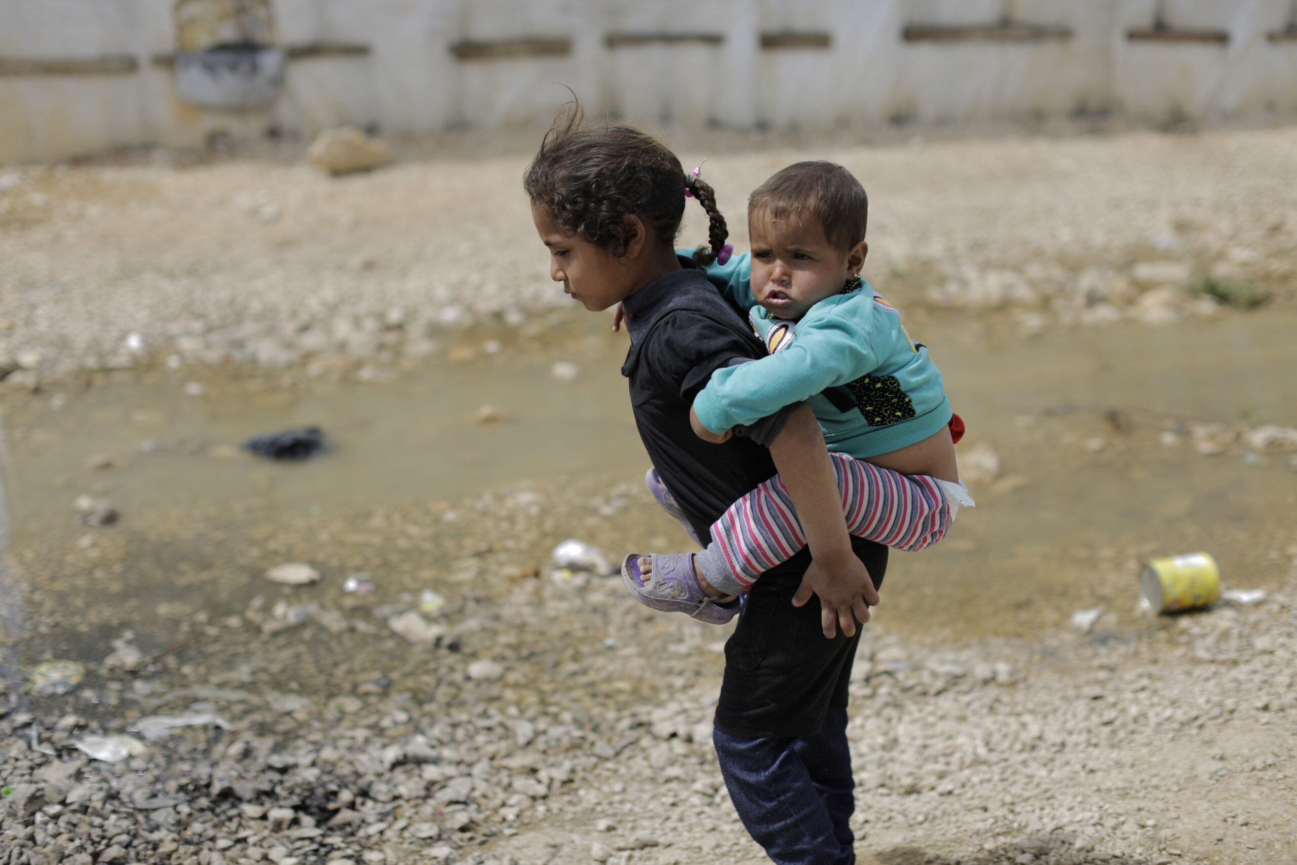 A Syrian refugee girl holds her brother as she walks at an informal refugee camp, at Al-Marj town in Bekaa valley, east Lebanon Lebanon, Saturday, April 8, 2017. For the millions of Syrian refugees scattered across camps and illegal settlements across the region, the chemical attack on a town in northern Syria and subsequent U.S. strike was a rare moment when the world briefly turned its attention to Syria, before turning away again. (AP Photo/Hassan Ammar) (AP Photo/Hassan Ammar)