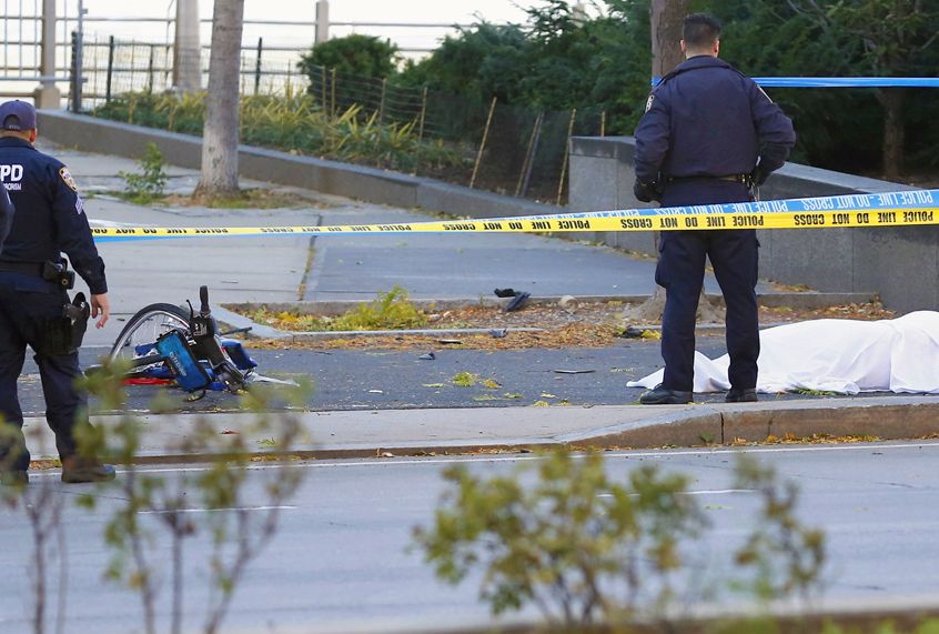 A New York Police Department officer stands next to a body under a white sheet near a mangled bike along a bike path, October 31, 2017 (AP/Bebeto Matthews)