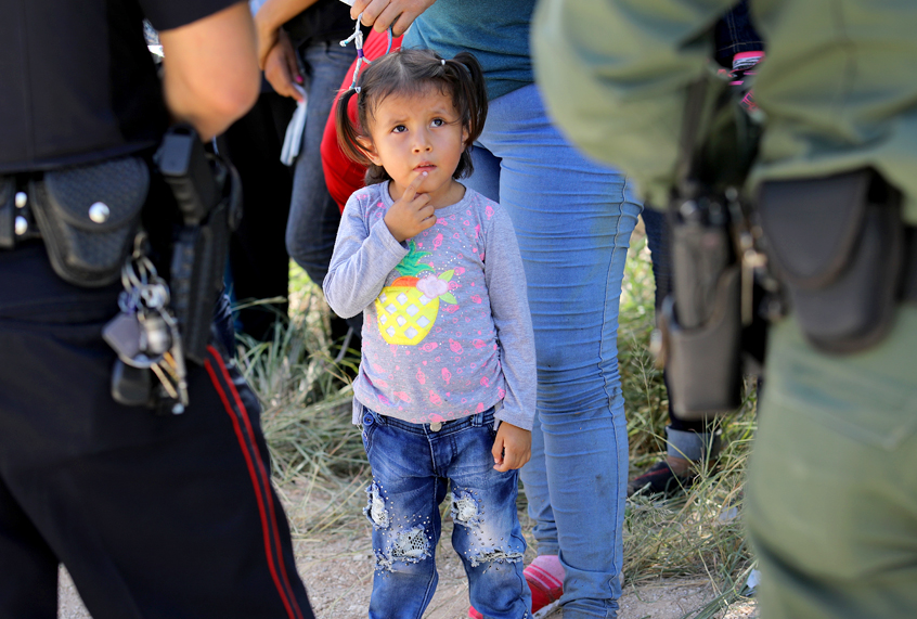 A Mission Police Dept. officer and a U.S. Border Patrol agent watch over a group of Central American asylum seekers before taking them into custody near McAllen, Texas. (Getty/John Moore)