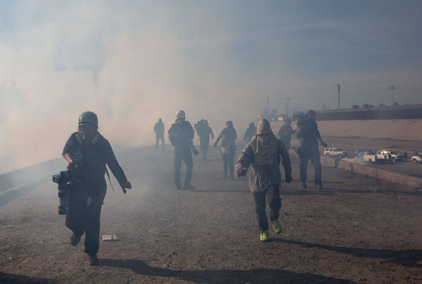 Migrants run from tear gas launched by U.S. agents after a group of migrants got past Mexican police at the Chaparral crossing in Tijuana, Mexico, Sunday, Nov. 25, 2018. (AP/Rodrigo Abd)