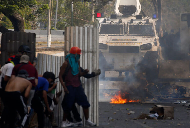 Opponents to Venezuela's President Nicolas Maduro stand behind makeshift shields as they face off with Bolivarian National Guards who are loyal to the president, during an attempted military uprising in Caracas, Venezuela, Tuesday, April 30, 2019. (AP/Ariana Cubillos)