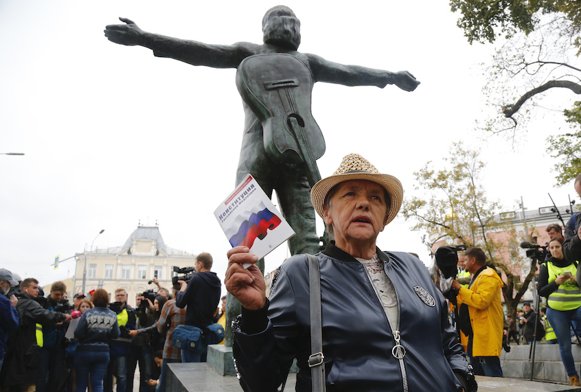 An opposition activist holds the Russian Constitution book in front of the monument to Soviet-era opposition legendary bard Vladimir Vysotsky during a protest in the center of Moscow, Russia, Saturday, Aug. 17, 2019. (AP Photo/Alexander Zemlianichenko)