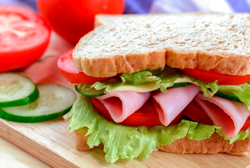 Close up of bologna sandwitcg on wooden board with cucumber and tomato (Getty/Mybona)