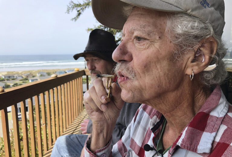 In this photo taken April 25, 2019, two-time cancer survivor and medical marijuana cardholder Bill Blazina, 73, smokes a marijuana joint on the deck of his neighbor’s home in Waldport, Ore. (AP Photo/Gillian Flaccus)