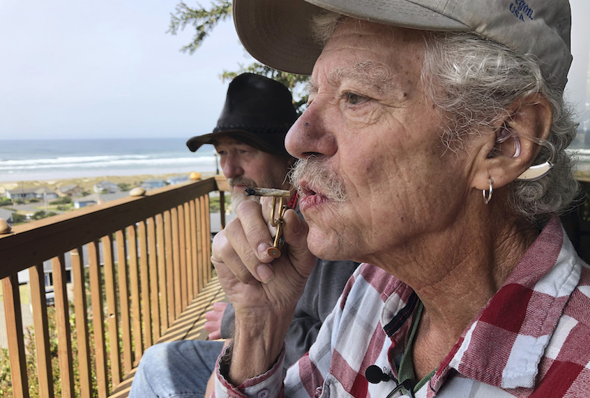 In this photo taken April 25, 2019, two-time cancer survivor and medical marijuana cardholder Bill Blazina, 73, smokes a marijuana joint on the deck of his neighbor’s home in Waldport, Ore. (AP Photo/Gillian Flaccus)