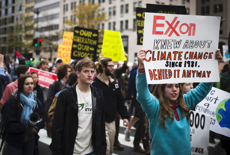 Climate activists demonstrate in Washington, D.C. in 2015. One displays a sign admonishing ExxonMobil for its complicity in furthering the climate apocalypse. (Johnny Silvercloud/Flickr)
