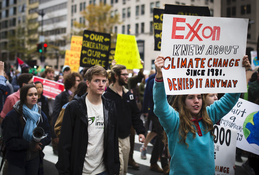 Climate activists demonstrate in Washington, D.C. in 2015. One displays a sign admonishing ExxonMobil for its complicity in furthering the climate apocalypse. (Johnny Silvercloud/Flickr)