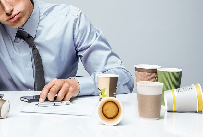 Distressed young man surrounded by empty cups of coffee (Getty Images)