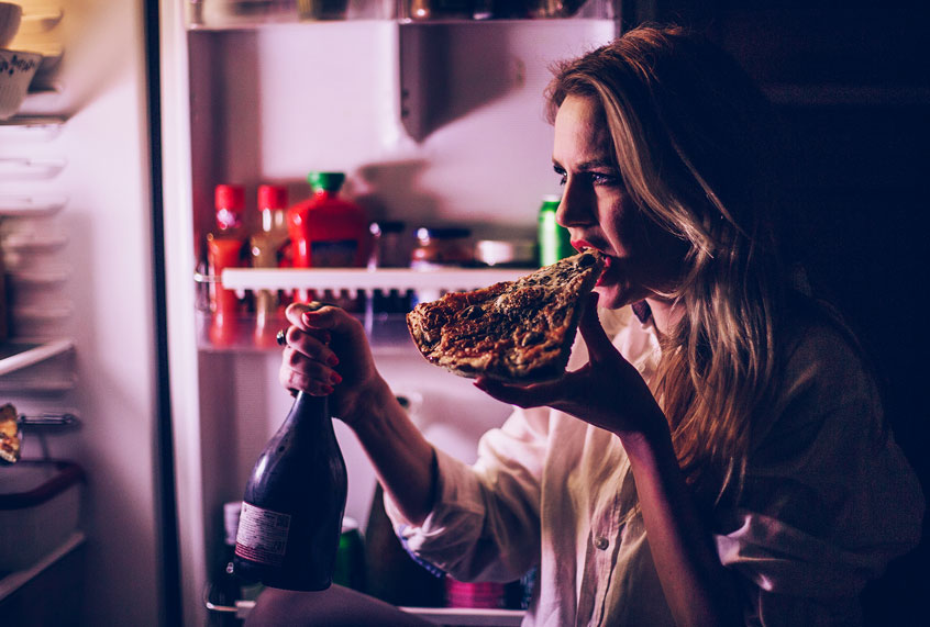 Woman eating pizza and drinking wine in front of the refrigerator during the night (Getty Images)