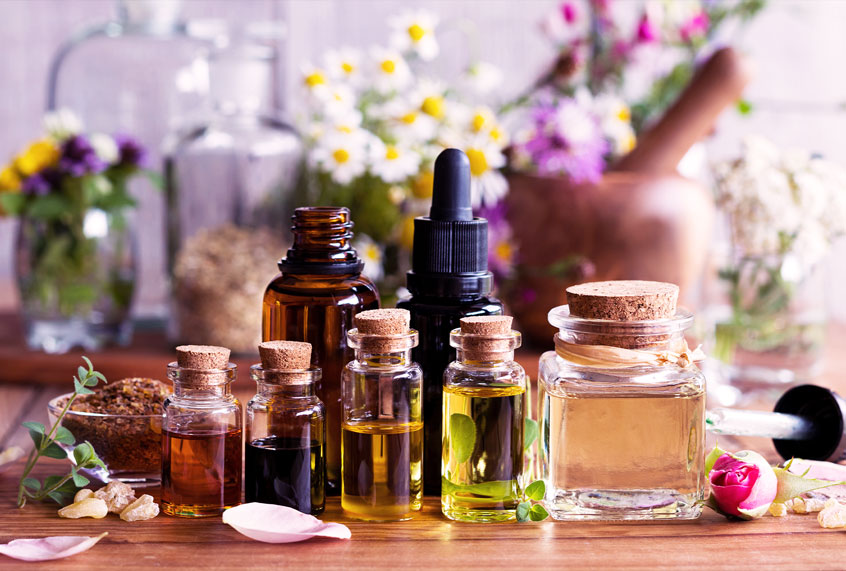 Selection of essential oils with various herbs and flowers in the background (Getty Images/Madeleine Steinbach)