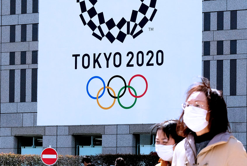 Pedestrians wearing face mask walk before the logo of the Tokyo 2020 Olympic Games displayed on the Tokyo Metropolitan Government building in Tokyo on March 24, 2020. (KAZUHIRO NOGI/AFP via Getty Images)