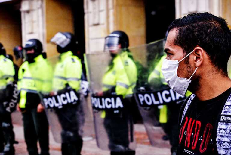 A person wearing a protective mask looks on as homeless, informal vendors, Venezuelan migrants and people displaced by the armed conflict protest demanding humanitarian aid during the COVID-19 quarantine. (Guillermo Legaria Schweizer/Getty Images)