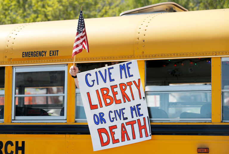 A person holds a sign while waving a flag in the direction of people gathered to voice their opposition to stay-at-home orders put into place due to the COVID-19 outbreak outside the Missouri Capitol (AP Photo/Jeff Roberson)