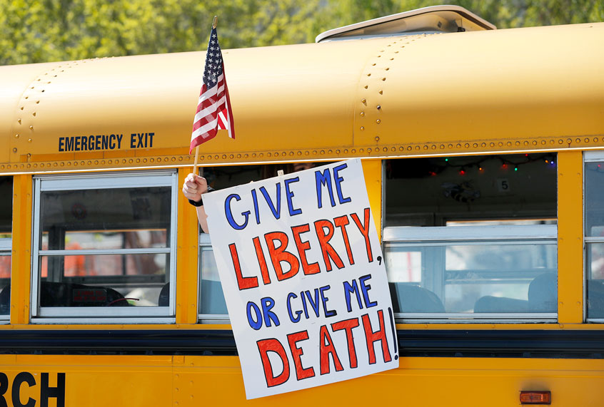 A person holds a sign while waving a flag in the direction of people gathered to voice their opposition to stay-at-home orders put into place due to the COVID-19 outbreak outside the Missouri Capitol (AP Photo/Jeff Roberson)