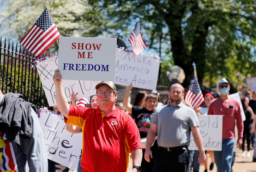 People hold signs as they walk past the governor's mansion to protest stay-at-home orders put into place due to the COVID-19 outbreak (AP Photo/Jeff Roberson)