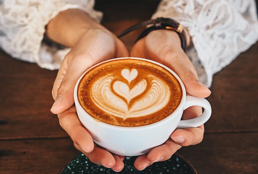 A woman's hands holding a cup of hot latte coffee in her hands (Getty Images)