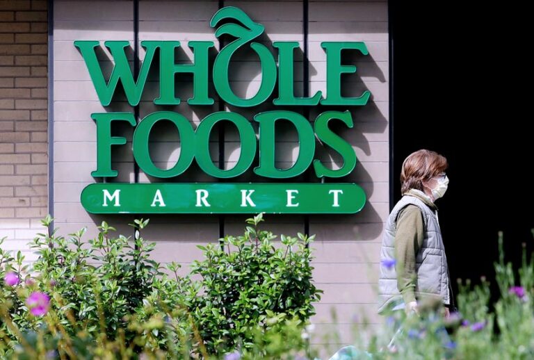 A pedestrian wears a mask while walking past a sign for a Whole Foods Market in San Francisco, Tuesday, March 31, 2020. (AP Photo/Jeff Chiu)