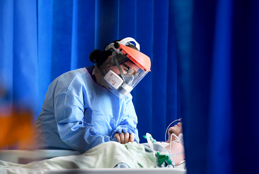 A member of the clinical staff wearing Personal Protective Equipment PPE cares for a patient with coronavirus in the intensive care unit at the Royal Papworth Hospital in Cambridge, England (Neil Hall/Pool via AP)