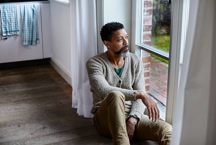 Pensive man sitting on the floor looking out of window (Getty Images/Oliver Rossi)
