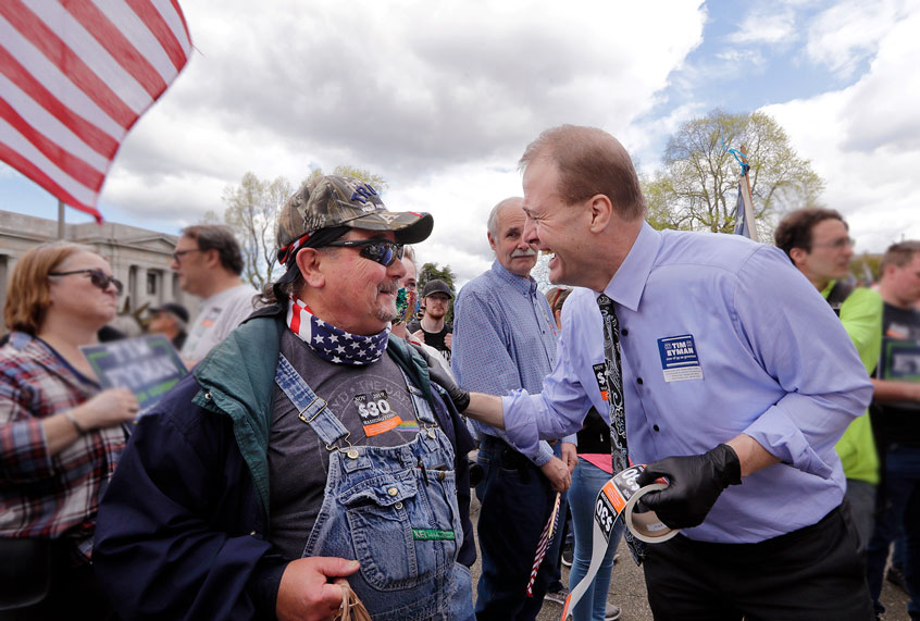 Gubernatorial candidate Tim Eyman, right, disregards social distancing guidelines as he leans in to talk with Chuck Slifko at a crowded protest opposing Washington state's stay-home order to slow the coronavirus outbreak Sunday, April 19, 2020, in Olympia, Wash. (AP Photo/Elaine Thompson)