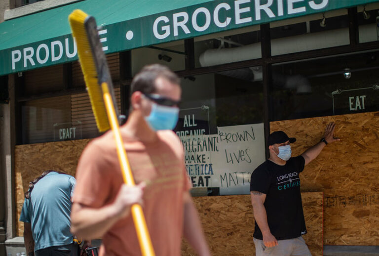A volunteer carrying a broom passes by a store being boarded up in Downtown Long Beach, California on June 1, 2020, after a night of protests and looting. (APU GOMES/AFP via Getty Images)