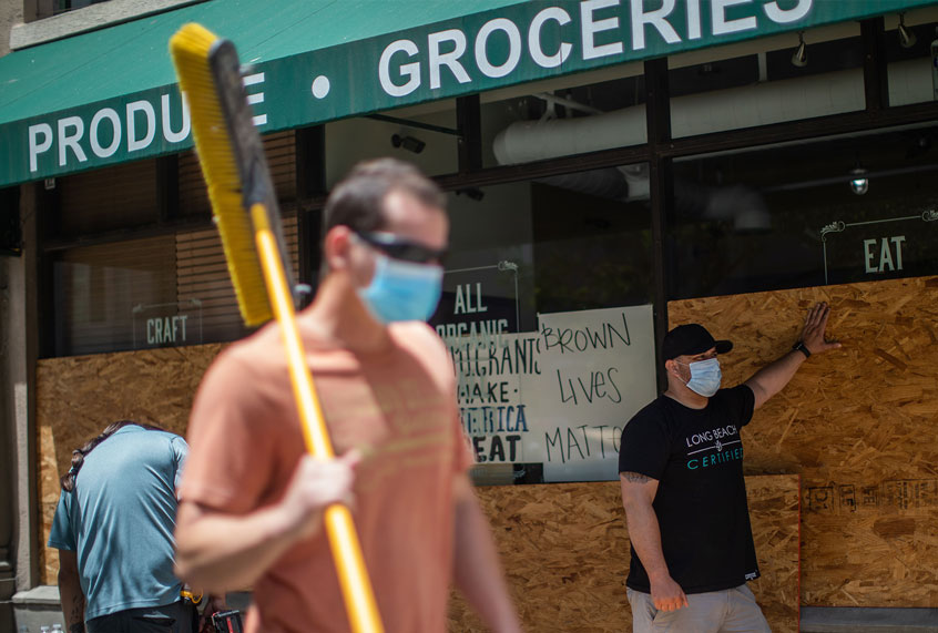 A volunteer carrying a broom passes by a store being boarded up in Downtown Long Beach, California on June 1, 2020, after a night of protests and looting. (APU GOMES/AFP via Getty Images)