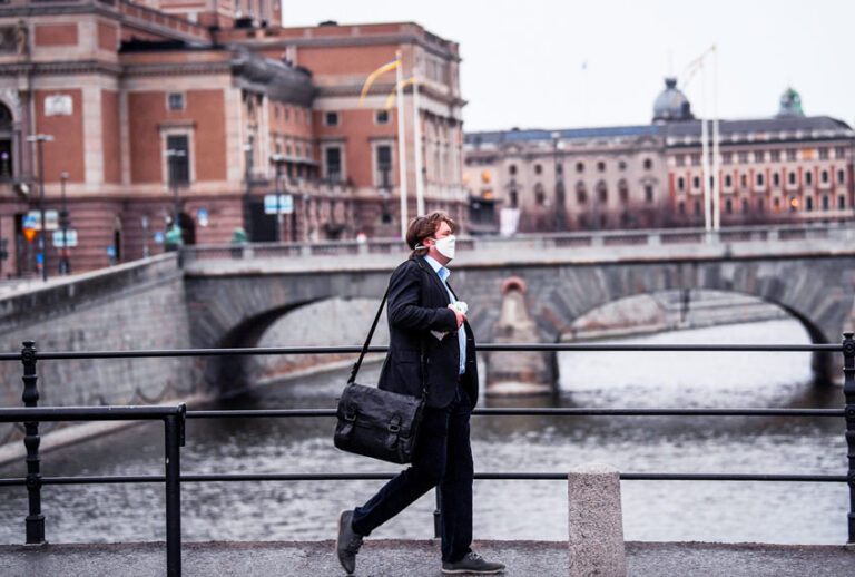 A man wearing a protective mask walk in the rain past the Royal Swedish Opera (at left) in Stockholm, Sweden (Getty Images)