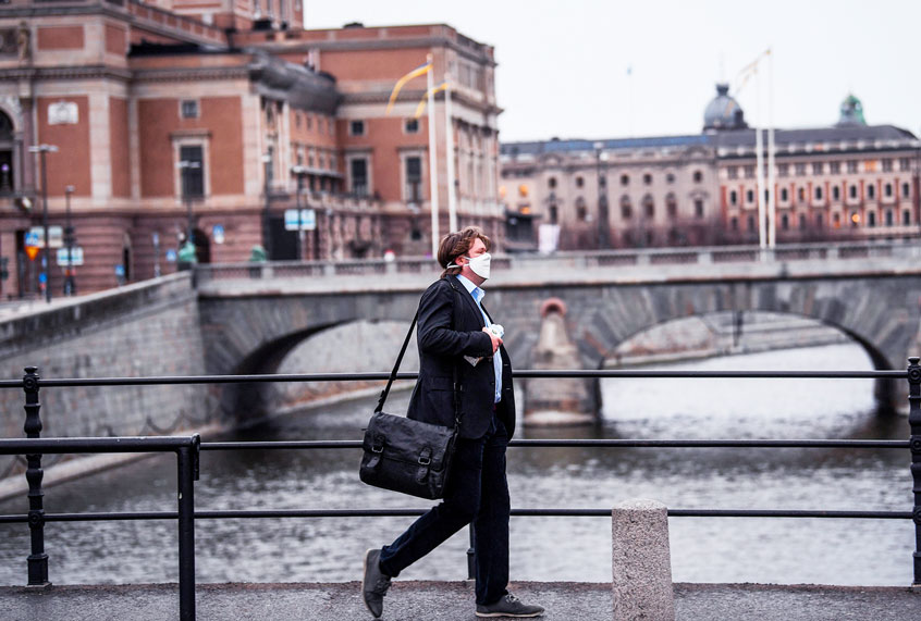 A man wearing a protective mask walk in the rain past the Royal Swedish Opera (at left) in Stockholm, Sweden (Getty Images)