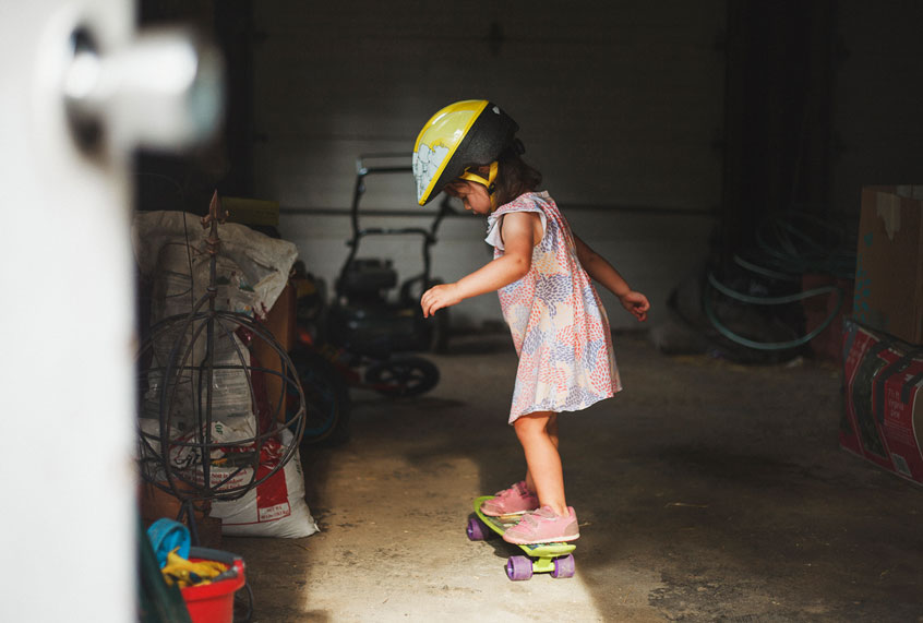 Side view of girl wearing helmet while standing on skateboard in garage (Getty Images)