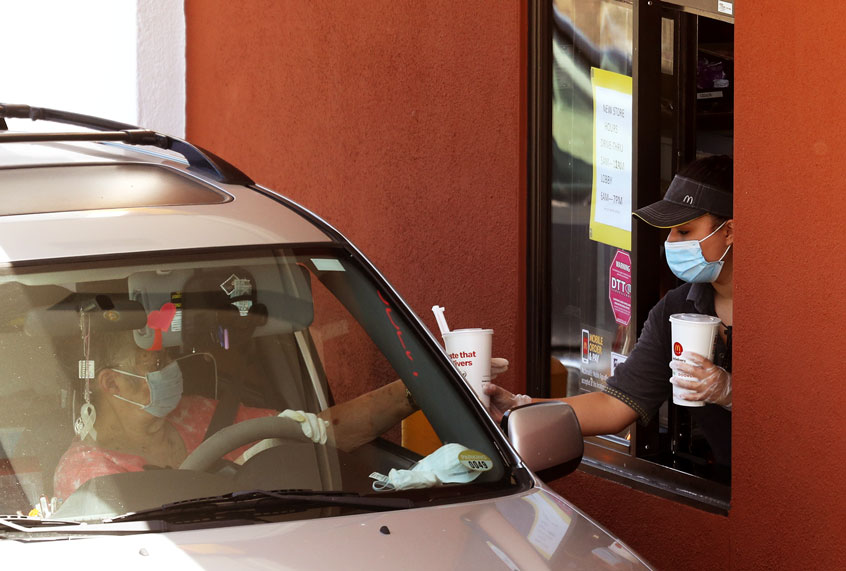 A worker wears a mask and gloves as she hands soft drinks to a customer at a McDonald's drive-thru on April 22, 2020 in Novato, California. (Justin Sullivan/Getty Images)