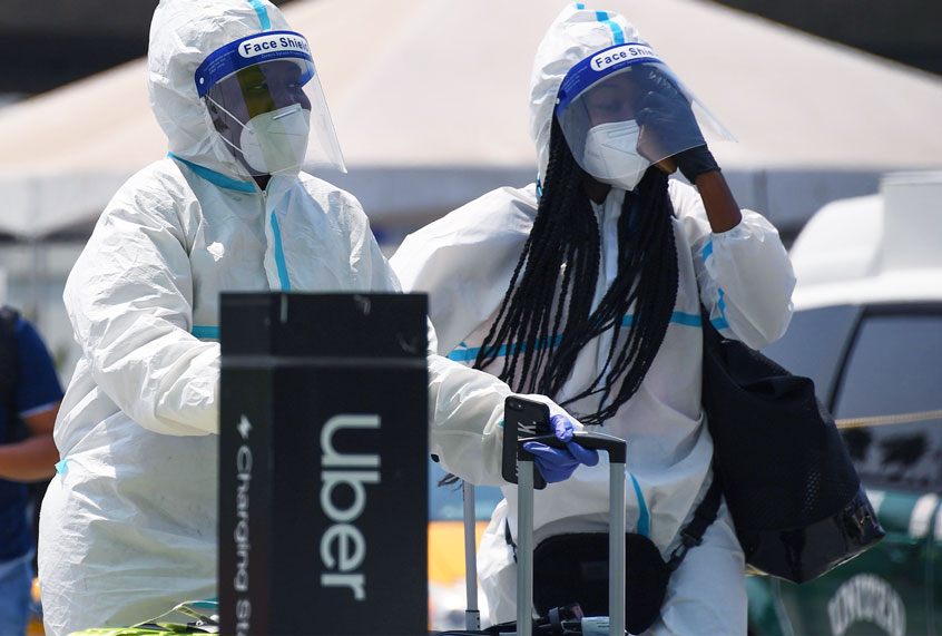 Travelers wearing protective suits, facemasks, face shields and gloves walk past an Uber pick up area August 20, 2020 at Los Angeles International Airport in Los Angeles, California. (ROBYN BECK/AFP via Getty Images)