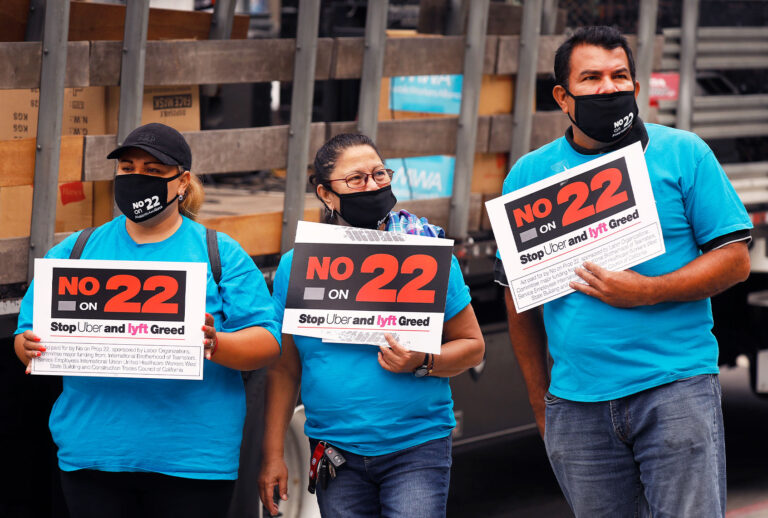 Luz Laguna, Isabelle Ramos and Leonardo Diaz, left to right, with Mobile Workers Alliance hold signs in support as app based gig workers held a driving demonstration with 60-70 vehicles blocking Spring Street in front of Los Angeles City Hall urging voters to vote no on Proposition 22, a November ballot measure that would classify app-based drivers as independent contractors and not employees or agents, providing them with an exemption from Californias AB 5. (Al Seib / Los Angeles Times)