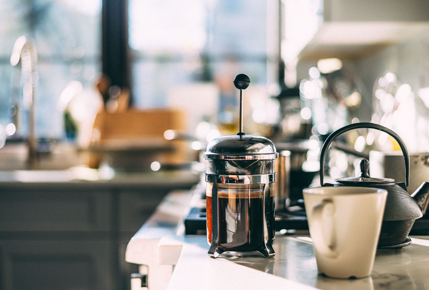 French press with coffee, teapot and mug on a kitchen counter on a sunlit morning (Getty Images)
