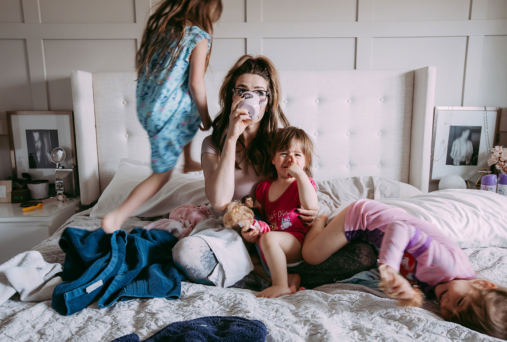 Stressed out mother sipping on a cup of coffee on her messy bed while her three daughters are playing around her (Getty Images)