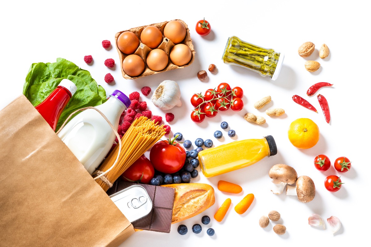 Top view of a paper bag full of canned food, fruits, vegetables, eggs, a milk bottle, berries, mushrooms, nuts, pasta, a chocolate bar and bread. (Getty Images)
