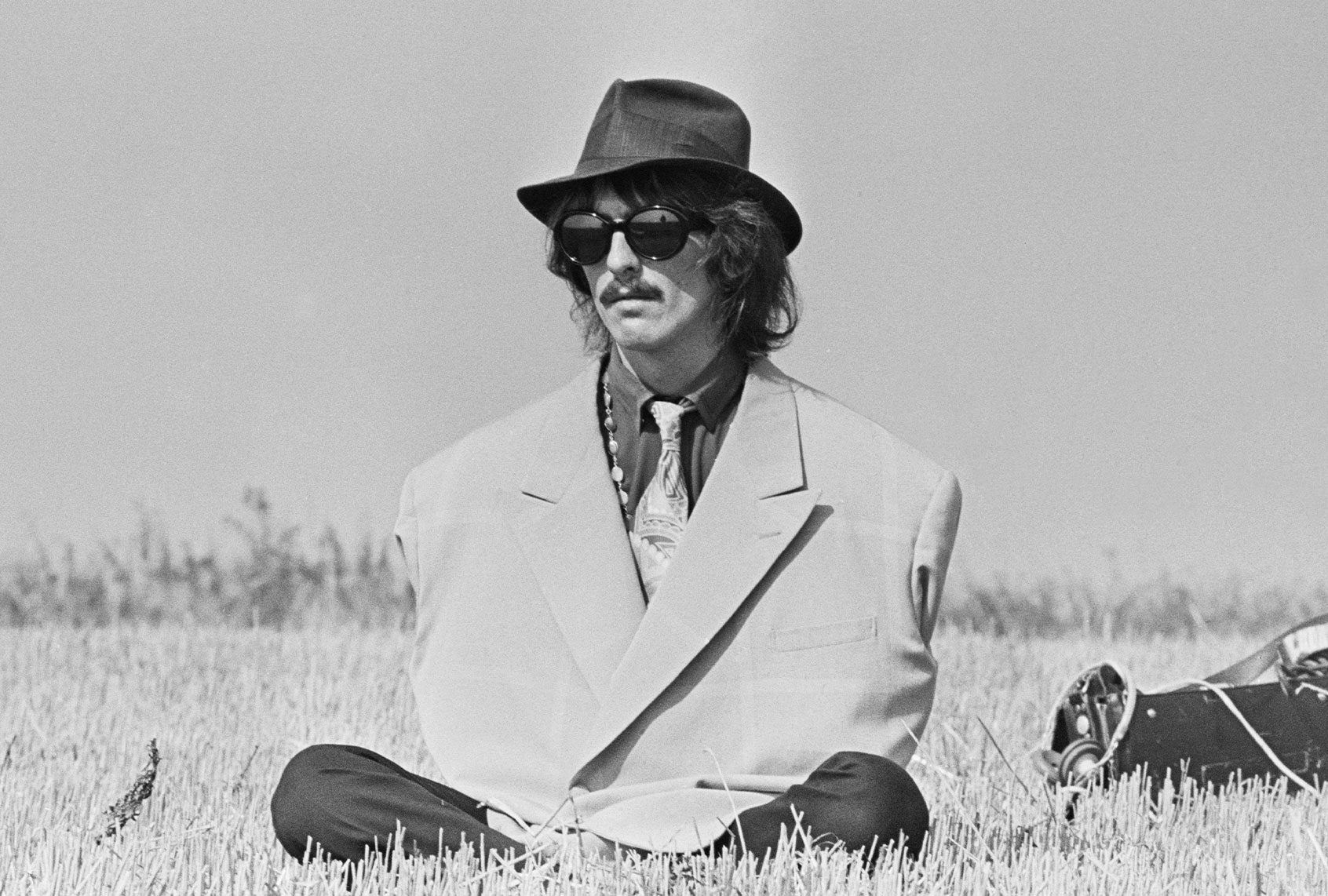 George Harrison (1943-2001), guitarist with the Beatles, pictured wearing an oversized jacket and a trilby hat during filming of 'Magical Mystery Tour' in a field near Newquay in Cornwall on 14th September 1967. (Chapman/Daily Express/Hulton Archive/Getty Images)