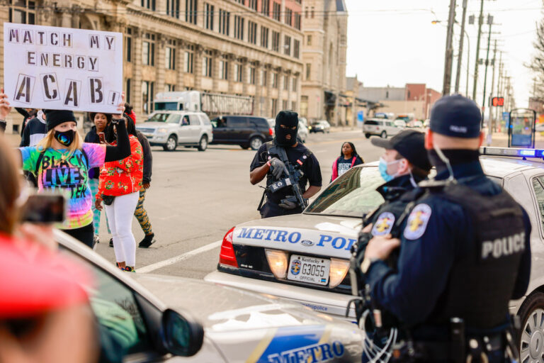 A protester holding a placard expressing her opinion in front of police during a memorial march to mark the one year anniversary since the Louisville Metro Police Department shot and killed Breonna Taylor at her home in Louisville. (Jeremy Hogan/SOPA Images/LightRocket via Getty Images)