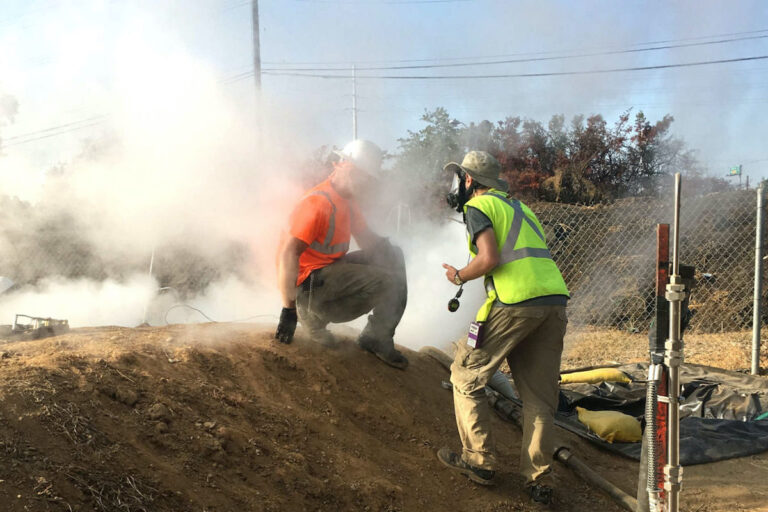 A worker, engulfed inside a plume created by the CIPP process, speaks with a researcher who wears a full face respirator to protect against chemical exposures. (Courtesy of Andrew Whelton / Undark)