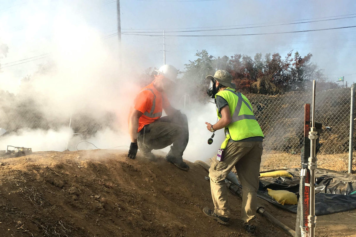 A worker, engulfed inside a plume created by the CIPP process, speaks with a researcher who wears a full face respirator to protect against chemical exposures. (Courtesy of Andrew Whelton / Undark)