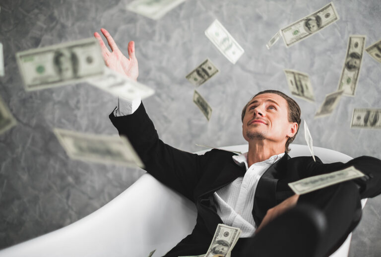 Man throwing dollar bills in a bathtub (Getty Images)