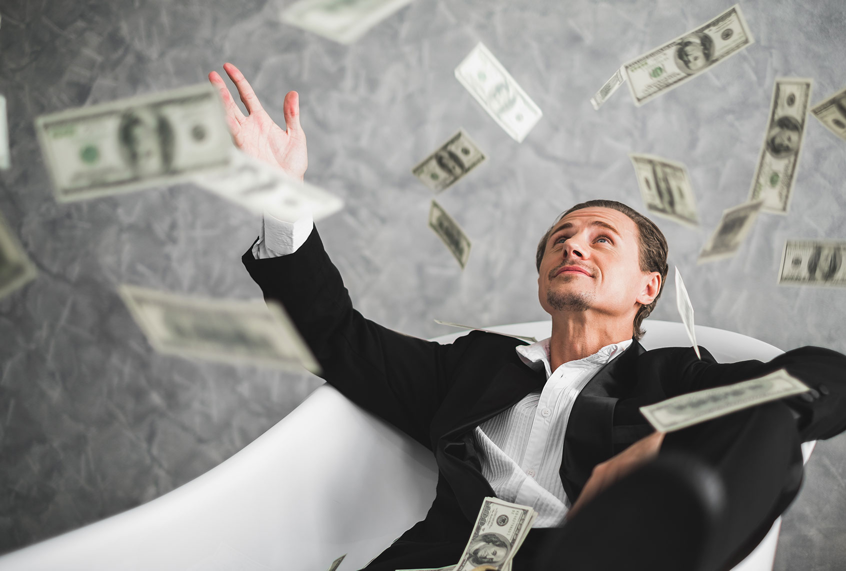 Man throwing dollar bills in a bathtub (Getty Images)
