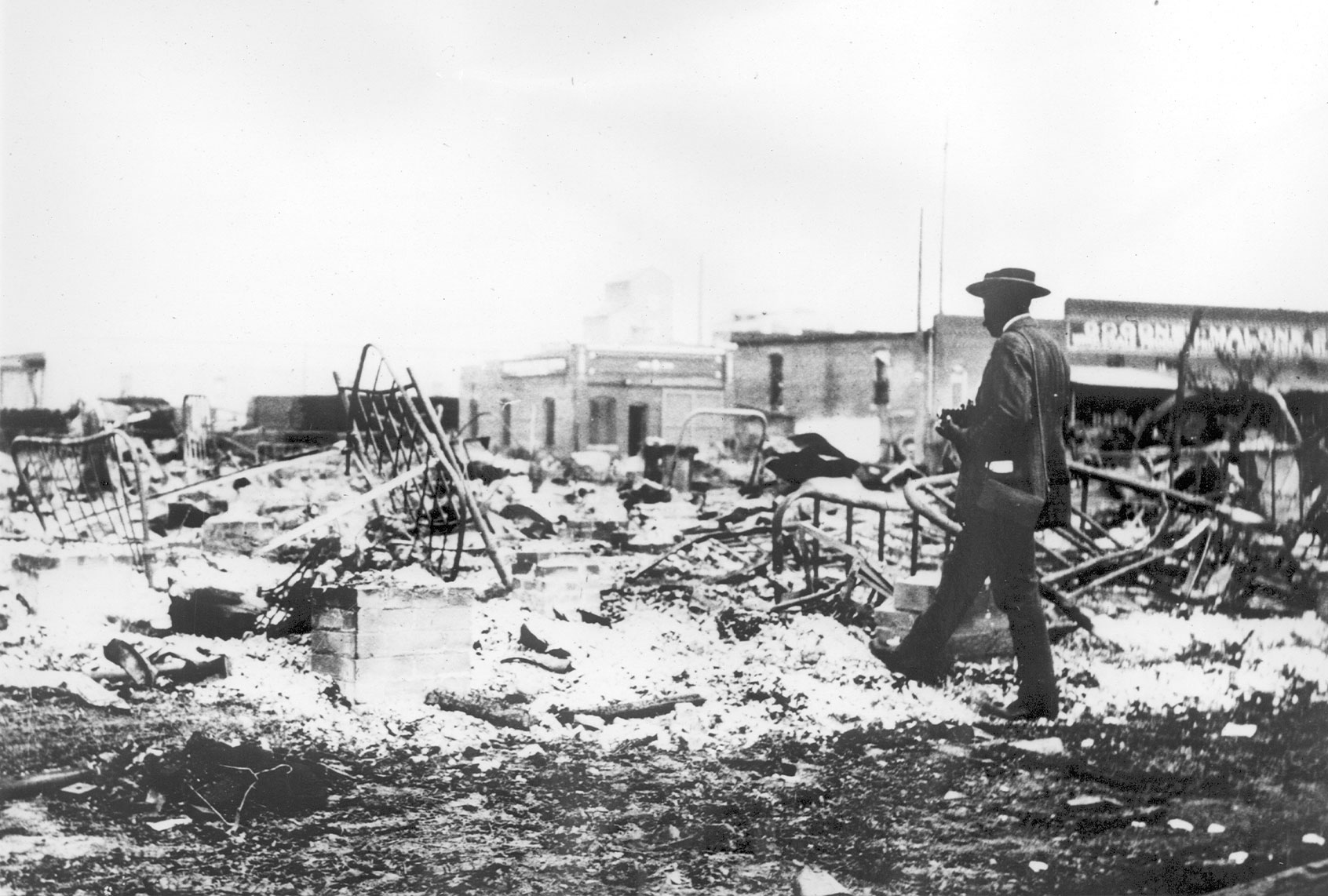 An African-American man with a camera looking at the skeletons of iron beds which rise above the ashes of a burned-out block after the Tulsa Race Massacre, Tulsa, Oklahoma, June 1921. (Oklahoma Historical Society/Getty Images)