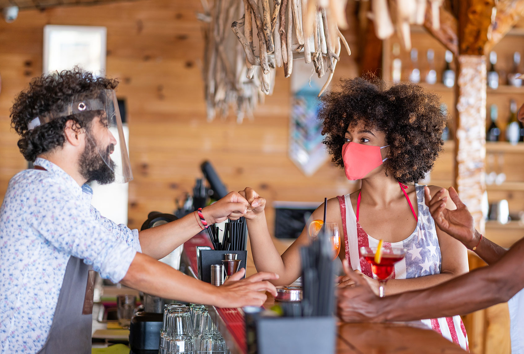 Friends drinking cocktail in a restaurant bar in summer days with protective face mask and practicing alternative greeting, during COVID-19 pandemic. (Getty Images)